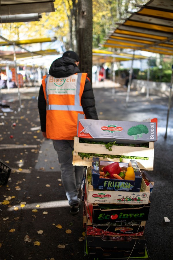 Un bénévole Biocycle de dos tire un ensemble de fruits et légumes récupérés au marché.