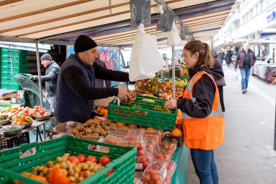Un commerçant sur le marché donne des fruits à une bénévole Biocycle