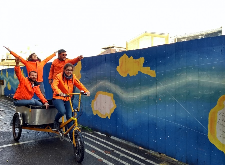 Les bénévoles Biocycle font le signe de la victoire, debout dans la remorque d'un vélo triporteur
